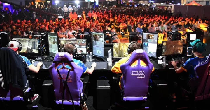 Excited gamers compete on stage at a lively Twitch gaming event, surrounded by a cheering audience and colorful banners.